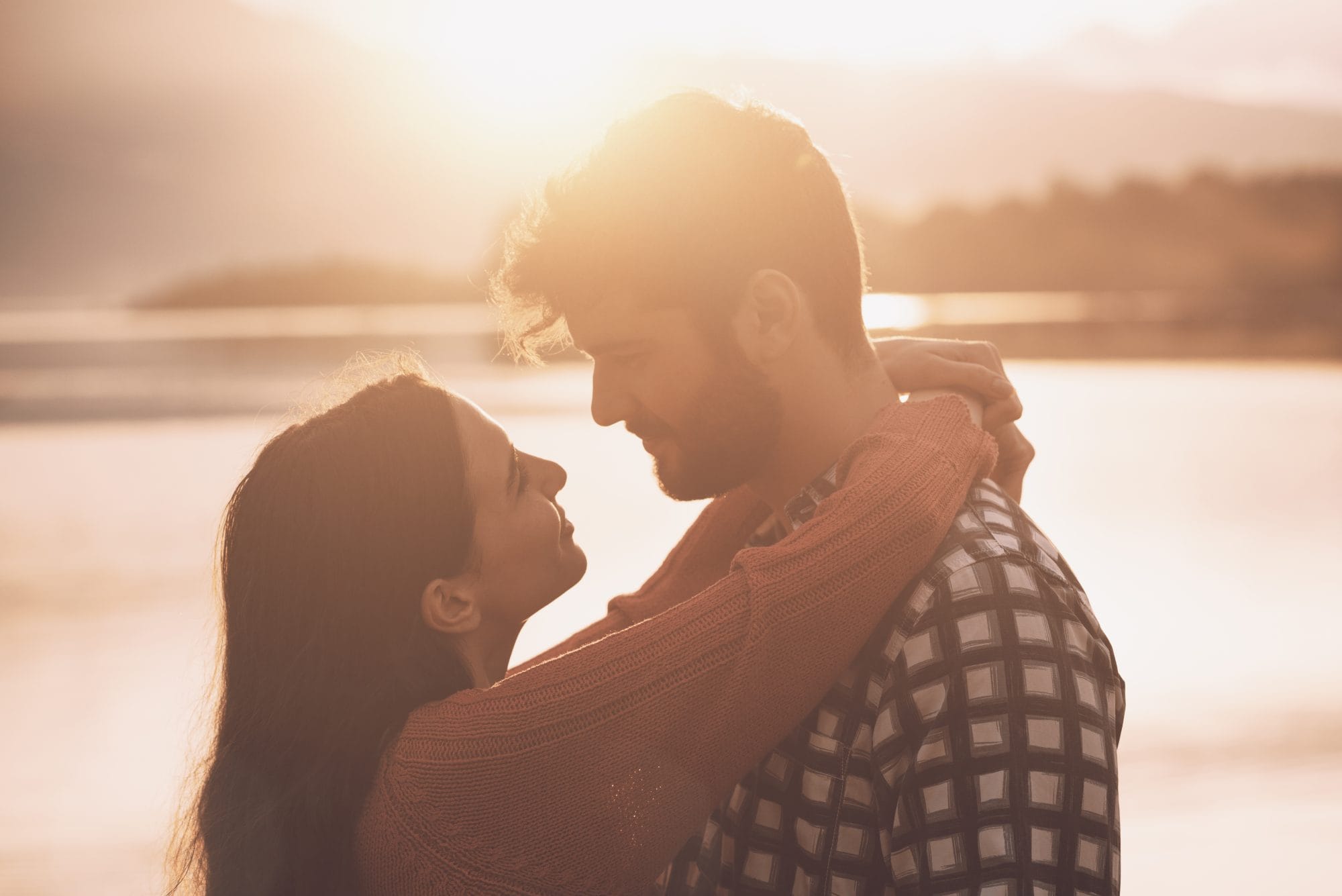 couple near lake embracing with sun in the background
