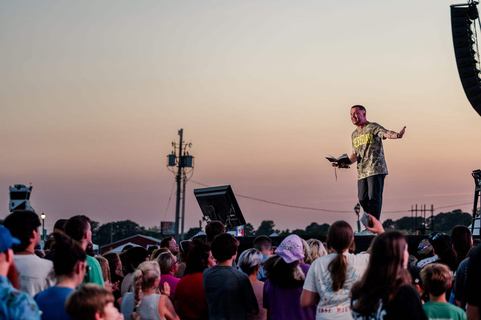 Man with Bible speaking to crowd at sunset