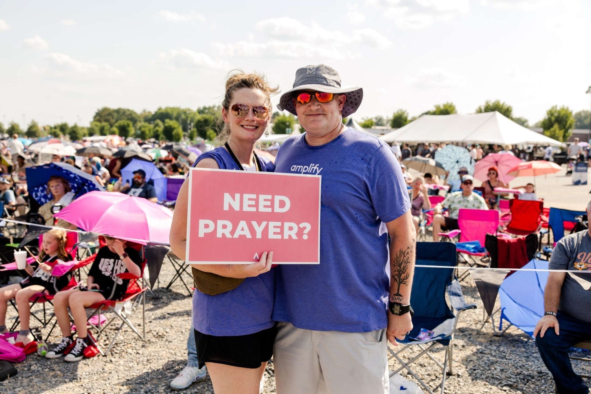 Man and woman holding a sign in a crowd that says "Need Prayer?"