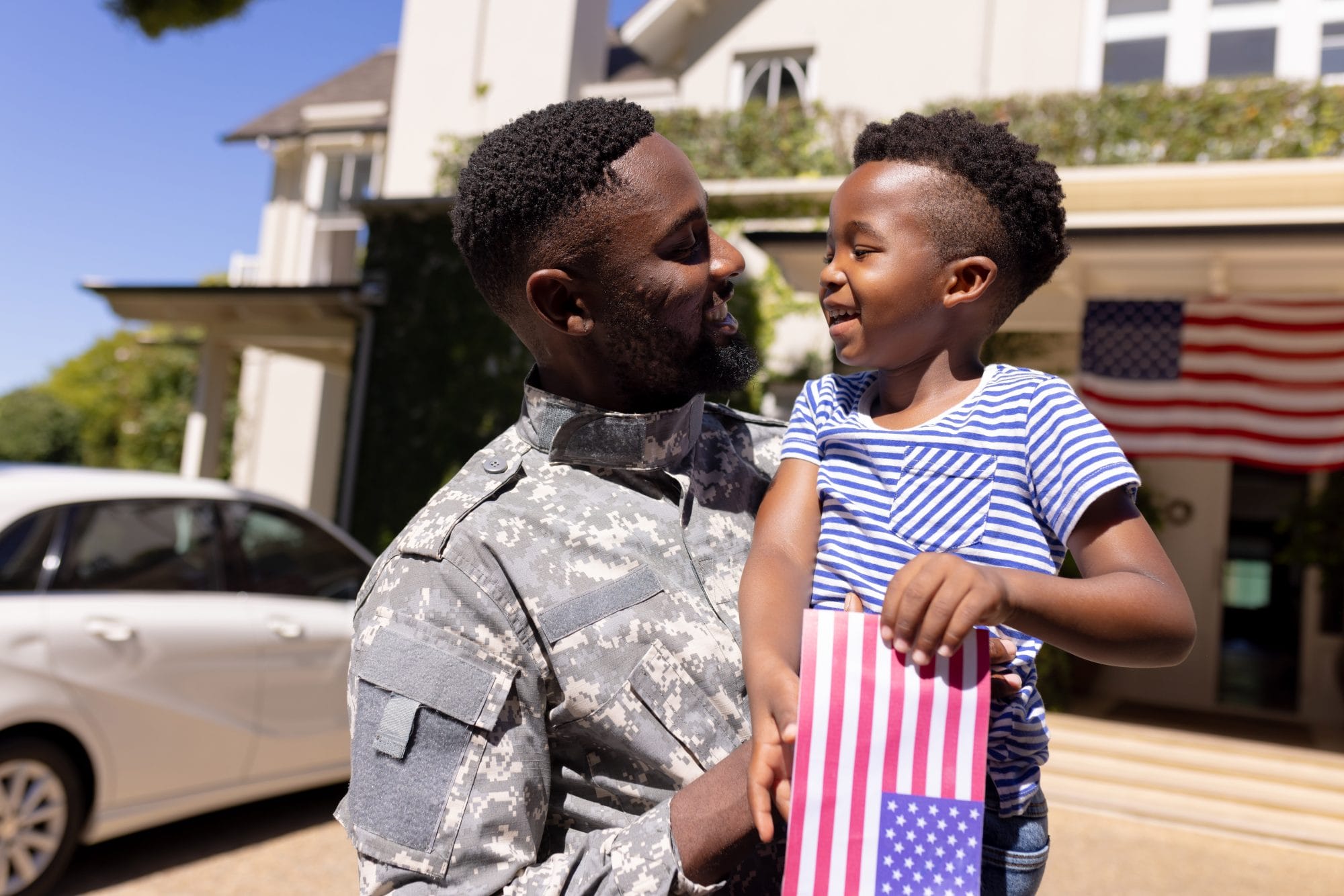 Black soldier holding his son in a driveway