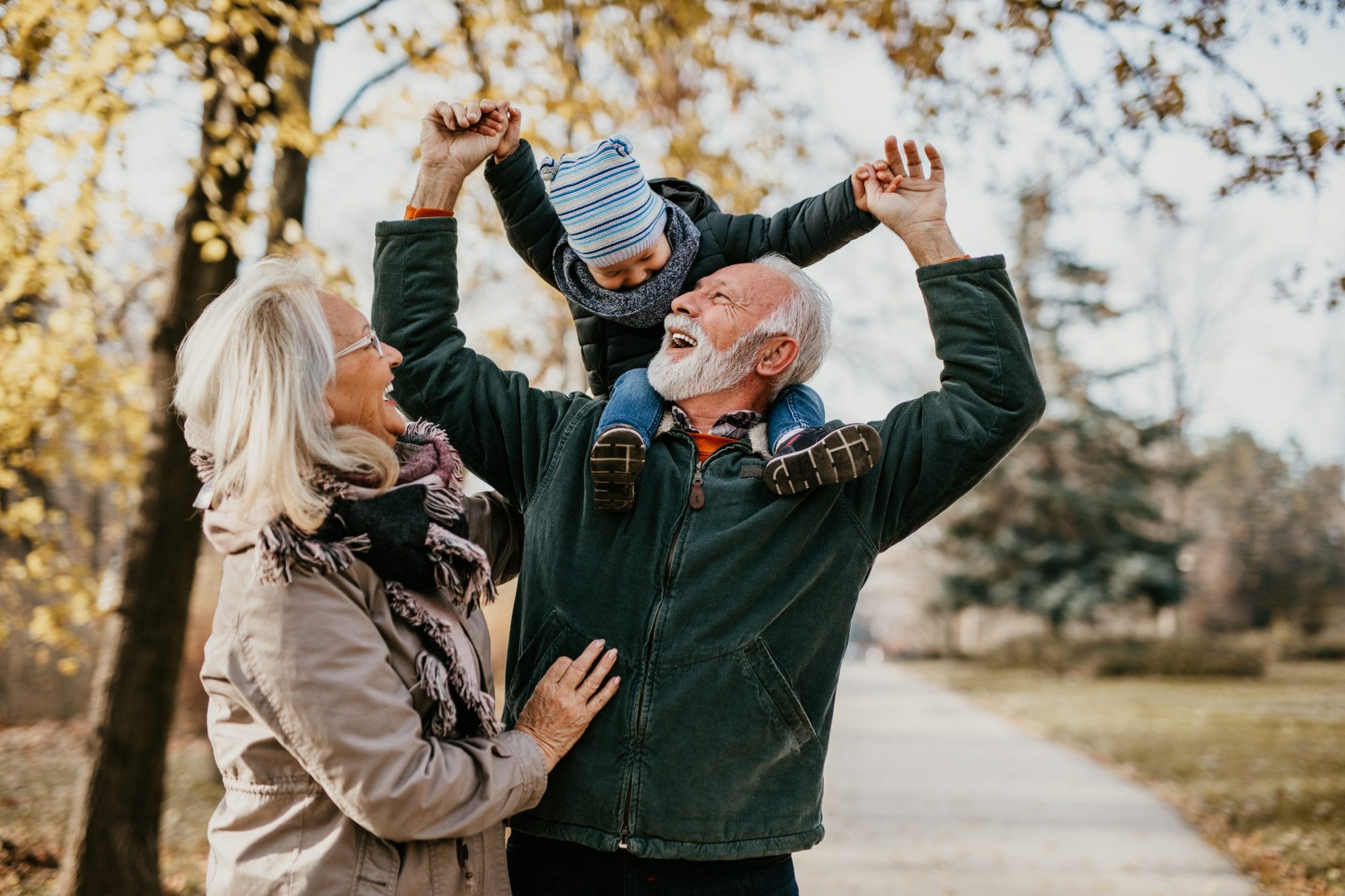 two grandparents with their grandson walking in a park and laughing