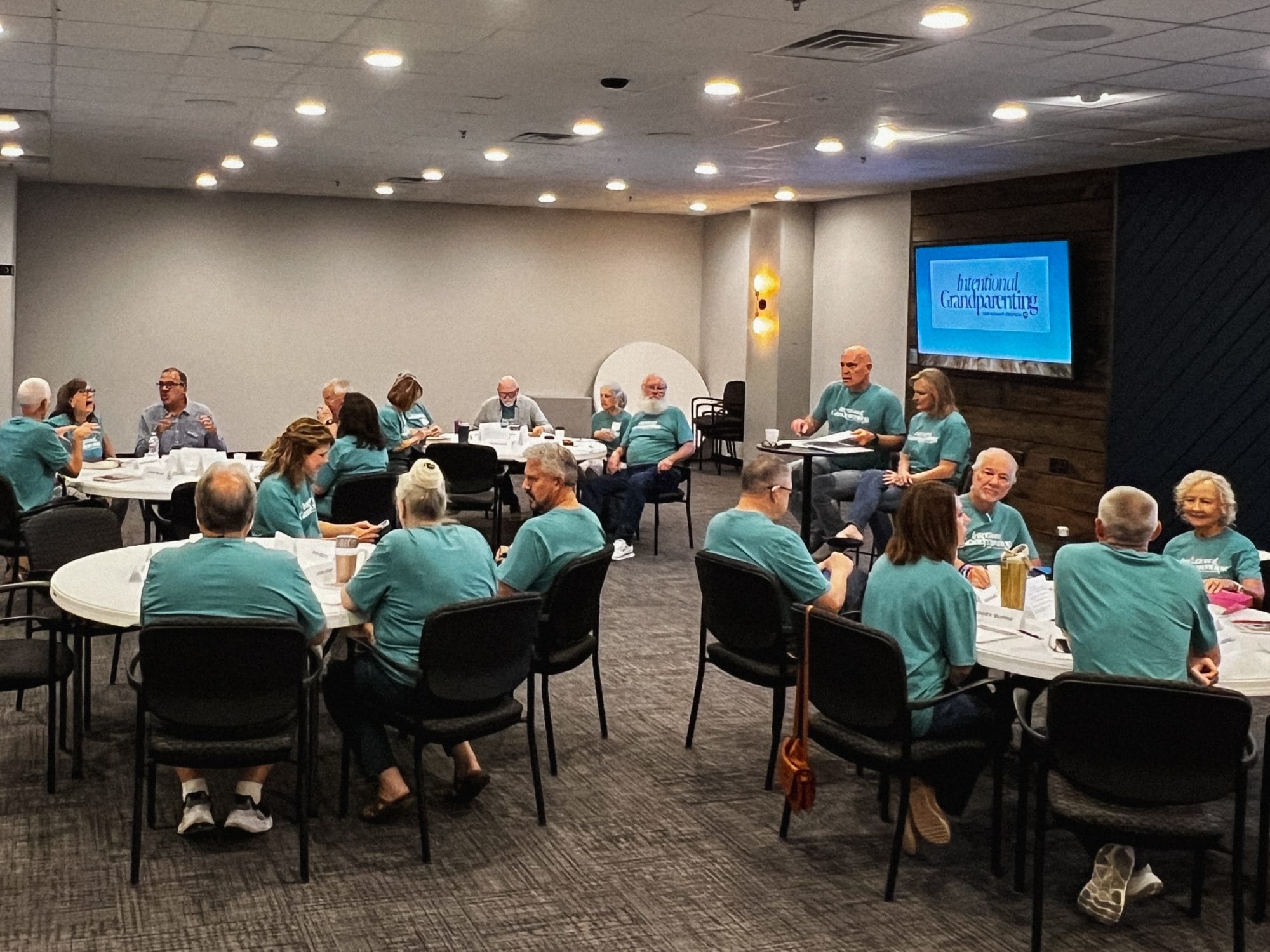 Group of older couples learning around tables in a meeting room for a local grandparents ministry 